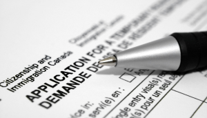 A close-up of a pen resting on a Canadian citizenship and immigration application form. The form includes English and French text, with APPLICATION FOR and DEMANDE DE visible.
