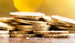 A close-up view of stacked gold coins with water droplets on their surfaces, set against a blurred yellow background.