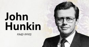 Memorial graphic with floral line art in the background. The text reads “John Hunkin, 1945–2025.” A black-and-white portrait of an older man wearing glasses and a suit appears on the right side.