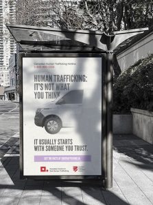 A bus stop advertisement shows a van and text reading: “Human Trafficking: It’s Not What You Think. It Usually Starts With Someone You Trust.” Contact info for the Canadian Human Trafficking Hotline is also visible.