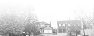 Two suburban houses with garages are seen on a quiet residential street. Trees, some leafless and some full, line both sides of the street. The image has a white, faded effect at the top and left side.