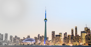 Toronto skyline at dusk with the CN Tower, lit blue, in the center. The left side of the image is in black and white, while the right side is in color, showing buildings and the Rogers Centre under a clear sky.